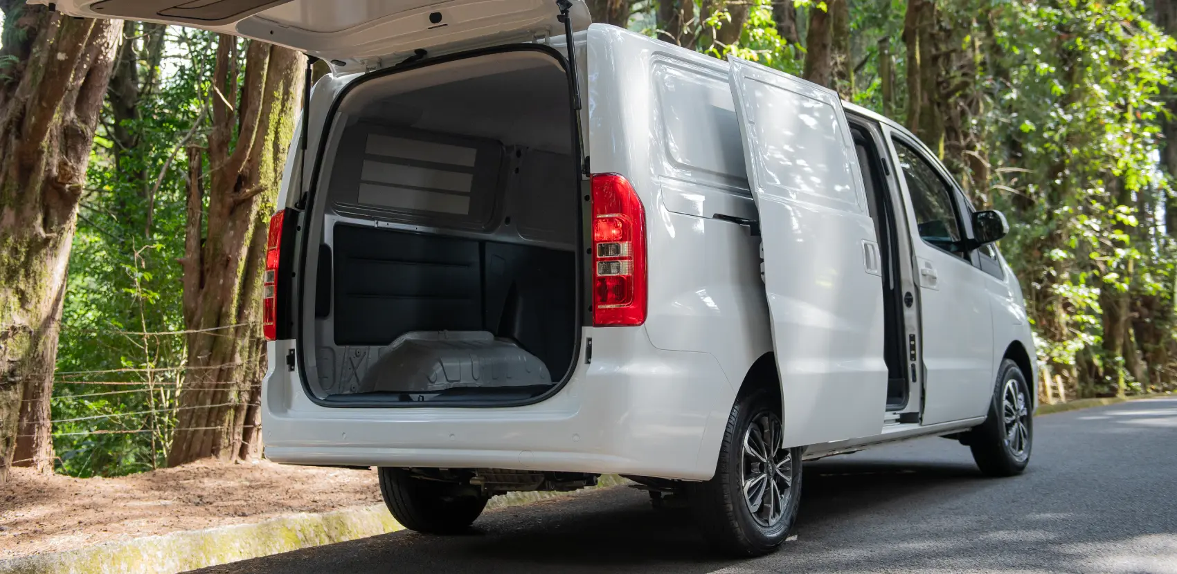Furgoneta eléctrica JAC con puertas abiertas, mostrando espacio interior, con vegetación de fondo.