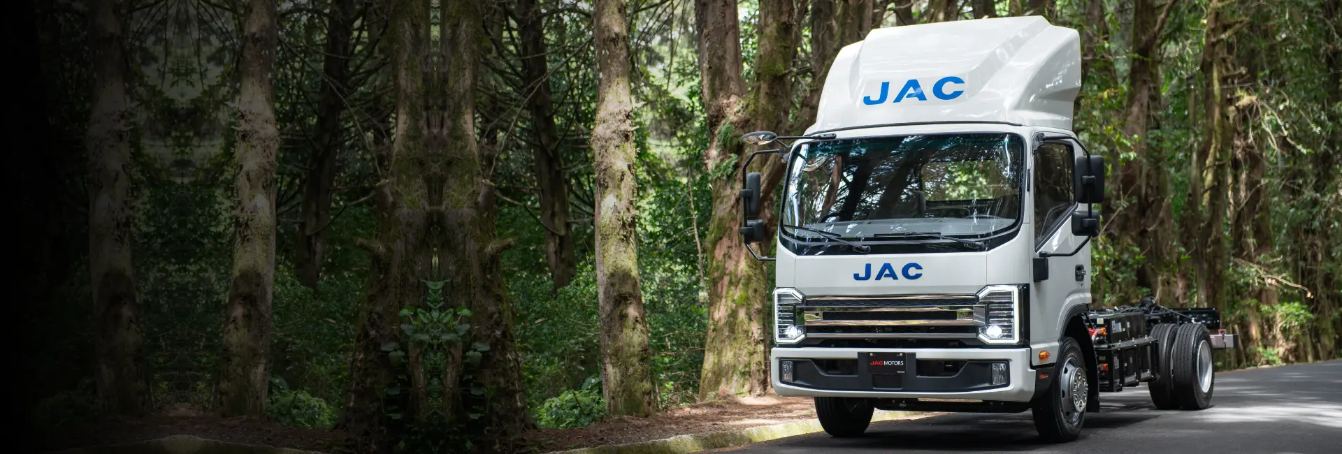 Camión eléctrico JAC en carretera con árboles de fondo.