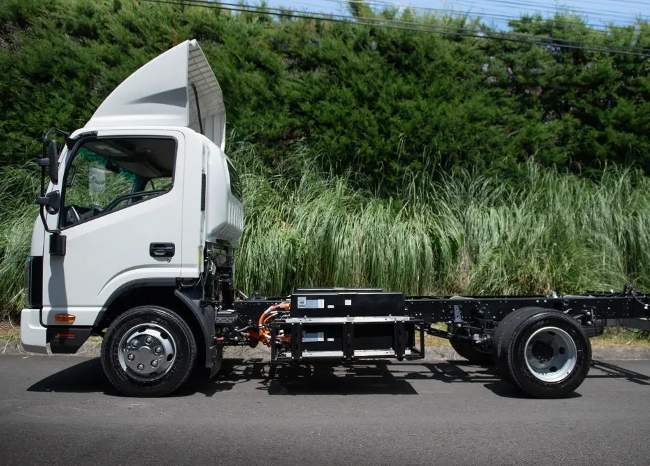 Camión eléctrico estacionado en camino rural con vegetación de fondo.