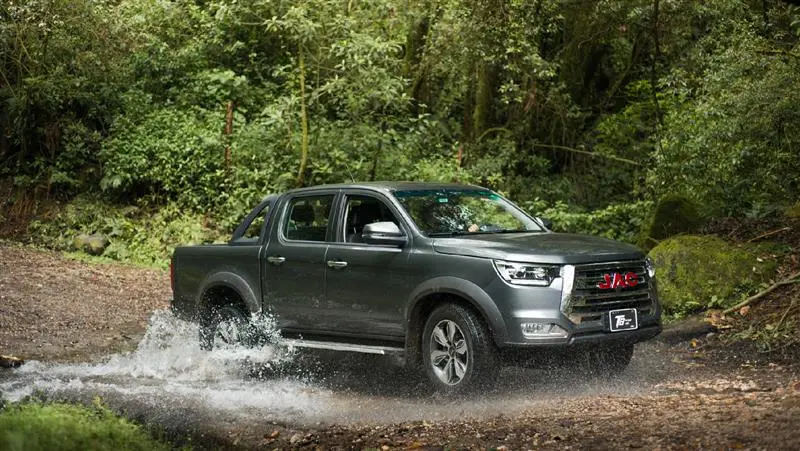 Modelo JAC T8 en terreno irregular con árboles de fondo.
